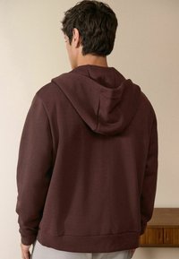 Burgunderfarbener Hoodie aus weichem Stoff, mit einer Kapuze mit Kordelzug, langen Ärmeln und einer lockeren Passform. Einfaches Design ohne sichtbare Muster.