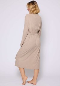 Beige wikkeljurk tot de knie met lange mouwen, een riem op de taille en een zijsplit; gemaakt van een zachte, rekbare stof met een gladde textuur.