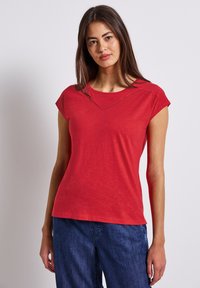 Červené tričko s krátkým rukávem a kulatým výstřihem, s jemným trojúhelníkovým výřezem na výstřihu, vyrobené z lehkého materiálu.