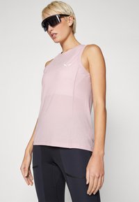 Sleeveless light pink athletic top with a round neckline, smooth texture, and a subtle logo detail on the chest, paired with dark leggings.