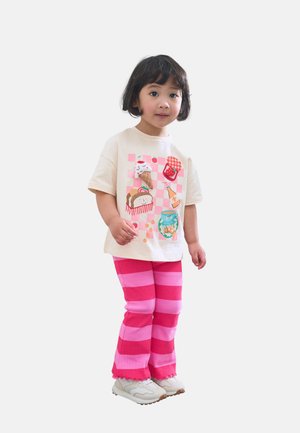 Krämfärgad grafisk t-shirt med färgglada matillustrationer, ihopparad med randiga byxor i rosa och magenta samt ljusa sneakers.