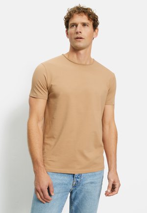 Hellbeige Kurzarm-T-Shirt aus glattem Stoff mit Rundhalsausschnitt und taillierter Passform, kombiniert mit hellblauen Jeans.
