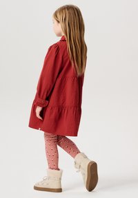 Röd, texturerad klänning med puffärmar och lager av volanger; matchad med rosa leggings med blommönster och tan, pälsfodrade stövlar.