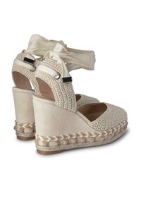 Sandales compensées tissées beige avec des lanières à lacets autour de la cheville, un tissu texturé et une semelle en espadrille tressée avec une base plate.