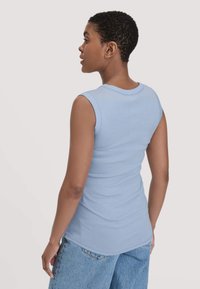 Helles blaues ärmelloses Oberteil aus weicher Baumwolle mit rundem Ausschnitt und figurbetontem Schnitt, kombiniert mit lockeren Denim-Shorts.