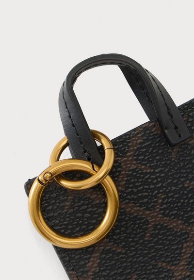 Gros plan d’un coin de sac à main noir texturé avec motif marron foncé, poignée en cuir noir et deux anneaux métalliques dorés entrelacés.
