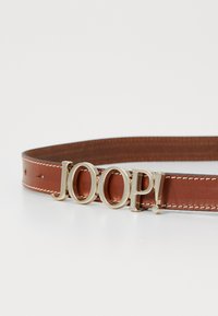 Ruskea nahkavyö, jossa on kultasävyinen "JOOP!" solki. Suora muoto, jossa näkyvät ommellut yksityiskohdat reunan ympäri.