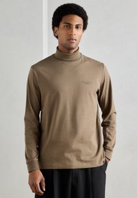 Pruun pikkade varrukatega kõrgekaelusega särk pehmest kangast, selge lõikega. Rinnal on peen logo ja soonikkäised.