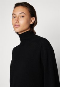 Schwarzer, gestrickter Rollkragenpullover mit lockerer Passform, strukturiertem Oberflächen und geripptem Kragen. Glattes Material, lange Ärmel und minimales Design.