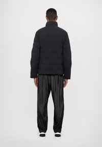 Black puffer jacket with a high collar, quilted texture, and an elastic hem. Paired with black, loose-fitting satin pants and white sneakers.