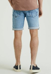 Pantaloni corti di denim azzurro chiaro con risvolti, due tasche posteriori e una texture sbiadita, abbinati a scarpe blu scuro con suola crema.