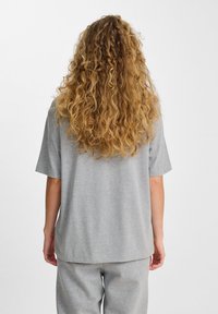 Camiseta de algodón gris con un corte relajado, mangas cortas y un dobladillo recto. El fondo es blanco liso, lo que resalta la textura de la prenda.