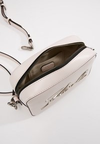 Jasnoróżowa skórzana torebka na ramię z zamkiem błyskawicznym na górze, dwukolorowym regulowanym paskiem i srebrnymi elementami wykończenia. Zawiera prostą kieszeń wewnętrzną.