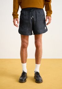 Svarta simbyxor med en texturerad mönstring, elastisk midja och snörning, tillsammans med svarta skor och vita strumpor.