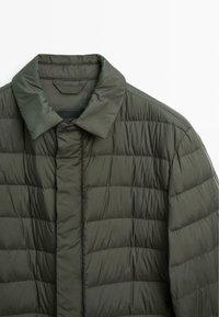 Padded jacket in dark green, featuring a quilted design, smooth texture, and a classic collar. Front closure without visible hardware.
