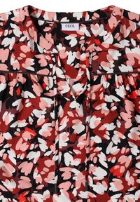 Blouse florale abstraite rouge, rose, blanche et noire avec col rond, liens à nouer et étiquette de marque "Cecil" au col.