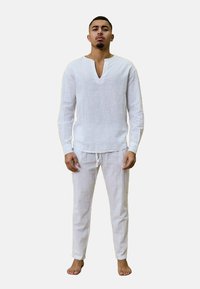 Tenue en lin blanc comprenant un haut à manches longues avec un décolleté en V profond et un pantalon à cordon. Texture douce, tissu léger et coupe décontractée.