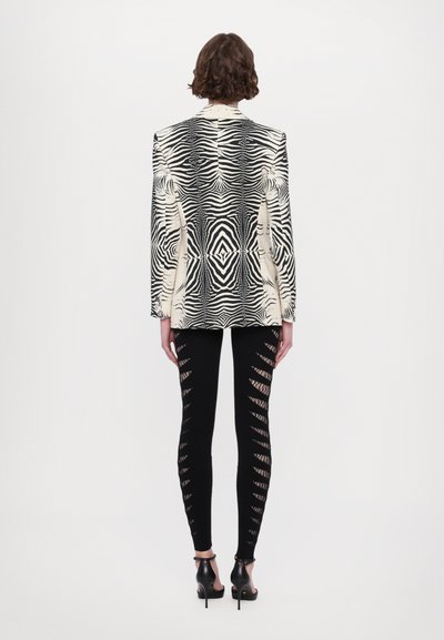 Zebra-mønstrede blazere i creme og sort, parret med sorte leggings med udskæringer langs siderne. Båret med hæle.