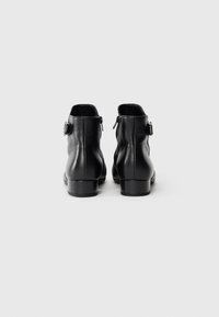 Black leather ankle boots with side buckles and low stacked heels shown from the back on a plain white background.