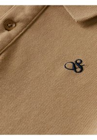 Polo marrón con una tela texturizada, que cuenta con un cuello abotonado y un logo bordado en navy en el pecho.