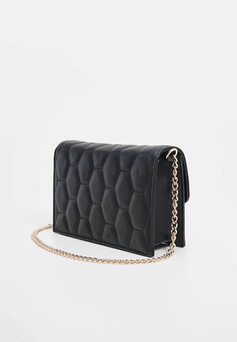 Clutch de piel acolchada negra con patrón hexagonal y correa de cadena dorada sobre un fondo blanco.