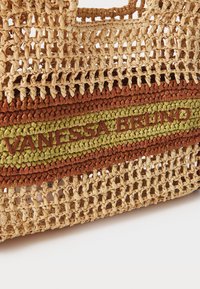 Geweven strohandtas met groene, bruine en oranje strepen, met "VANESSA BRUNO" geborduurd in bruin op een groene achtergrond.