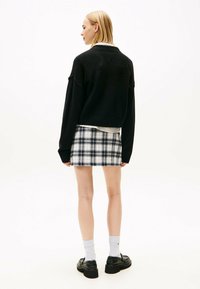 Schwarzer oversized Pullover mit geripptem Saum, über einem weißen Button-Up-Hemd getragen. Kurzer Karorock in Schwarz und Weiß, kombiniert mit schwarzen Plateauschuhen.