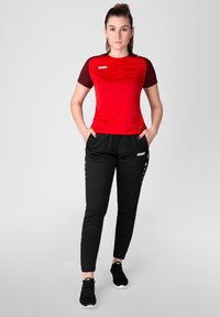 Rode sporttop met zwarte gestreepte mouwen, gecombineerd met zwarte joggingsbroek met accentdetails aan de zijkant en aansluitende manchetten, compleet met zwarte sneakers.