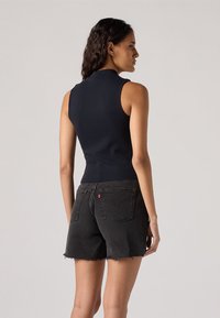 Top senza maniche blu navy con un collo alto, abbinato a pantaloni corti in denim neri con orli sfilacciati e tasche posteriori con dettagli di cucitura.