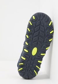 Podešev boty v tmavě šedé barvě s texturovaným vzorem a žlutými akcenty. Vyrobená z gumy, s hlubokými drážkami pro trakci a stabilitu.