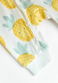 Dragkedjebodysuit i vit tyg med gula ananaser och gröna blad, med ribbade ärmslut och en slät yta.