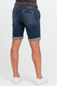 Jeansshorts med mörk tvätt, uppvikta fållar och ett flätat brunt bälte. Har bakfickor och strukturerad tyg för komfort.
