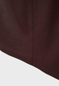 Tessuto in pelle borgogna con una superficie liscia e cuciture visibili lungo il bordo, realizzato con un design minimalista e linee pulite.