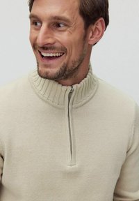 Beige zip-up tröja med ribbat krage, stickad struktur, halvdragkedja fram och avslappnad passform. Slät tyg och avslappnad design.