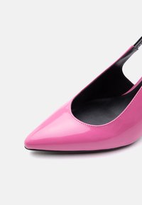 Γυαλιστερό ροζ μυτερό παπούτσι με λουρί στον αστράγαλο, μαύρη εσωτερική επένδυση και χαμηλό τακούνι σε λευκό φόντο.