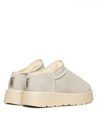 Zapatos slip-on de ante beige con un forro suave, suela gruesa beige y un pequeño logo en el talón para un detalle añadido.