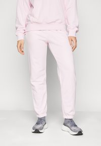 Lyser�øde sweatpants med elastiske manchetter, lavet af blødt stof, parret med grå sportssko med et struktureret design og hvid sål.