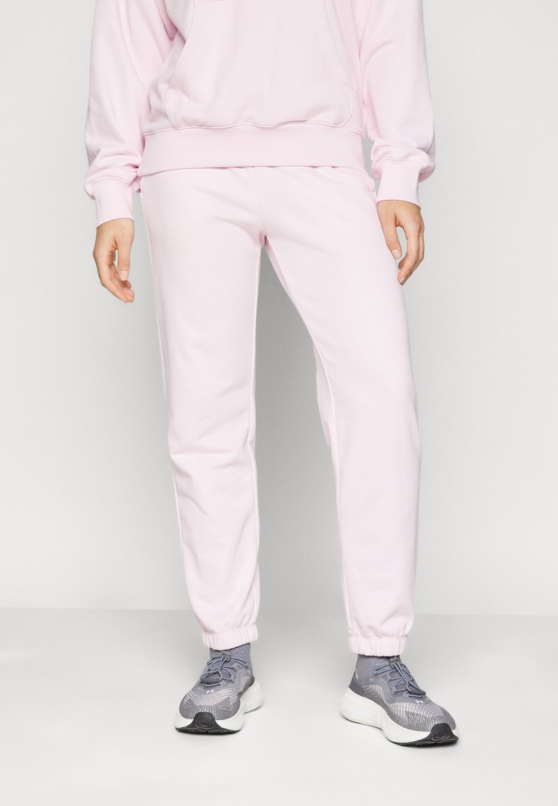 Lyserøde sweatpants med elastiske manchetter, lavet af blødt stof, parret med grå sportssko med et struktureret design og hvid sål.
