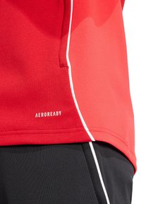 Rotes Sporthemd mit AEROREADY-Branding, mit glatter Textur und weißen Besätzen an der Seite. Kombiniert mit schwarzem Material darunter.