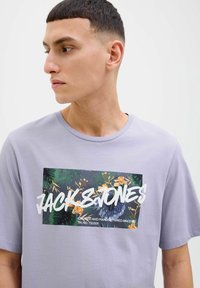 Světle fialové tričko s grafickým potiskem s tropickými listy a květinovými akcenty. Výrazné logo "JACK & JONES" v tučném bílém písmu.