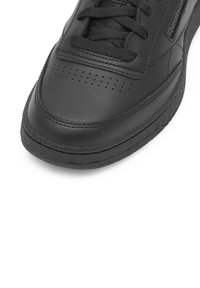 Juodi odiniai sportbačiai suapvalinta nosyte, subtiliai perforuotu viršumi ir tekstūruotu juodu guminiu padu. Komplekte yra plokščios juodos raištelės.