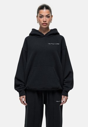 Schwarzer Hoodie mit großer Vordertasche und Kapuze mit Kordelzug, mit weißem gesticktem Text auf der Brust. Weicher Stoff und übergroßer Schnitt.