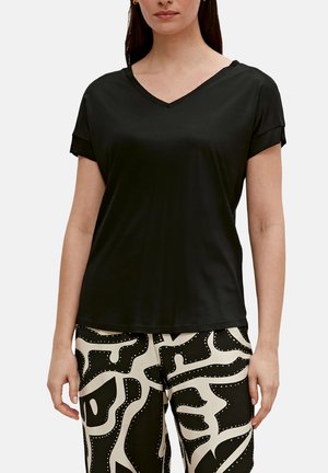Schwarzes kurzärmliges V-Ausschnitt-T-Shirt aus glattem Stoff. Mit umgeschlagenen Ärmeln und lockerer Passform. Kombiniert mit gemusterten Schwarz-Weiß-Hosen.