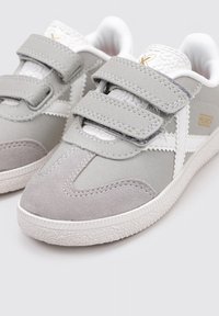 Zapatillas de ante y cuero grises con acentos blancos, que cuentan con dos correas de Velcro y detalles texturizados en la lengüeta. Suela de goma.