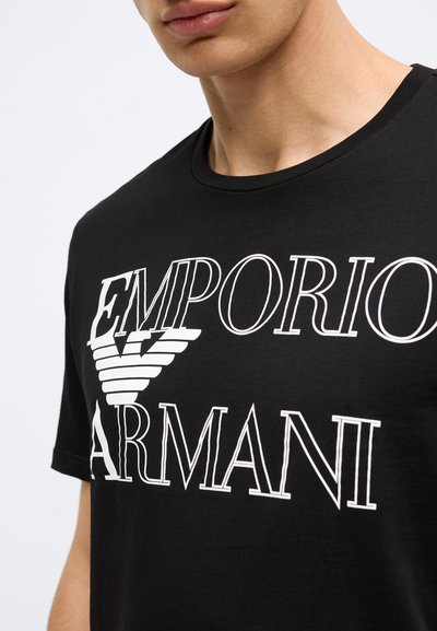 Čierne bavlnené tričko s veľkým bielym nápisom "EMPORIO ARMANI" a štýlovým logom. Mäkká textúra a klasický okrúhly výstrih.