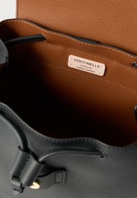 Interior de mala preta em couro com um forro castanho. Apresenta uma etiqueta com a inscrição "Coccinelle" e "Autêntico Couro Italiano." Acabamento texturizado.