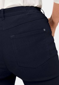 Donkerdenim jeans met een achterzak met een zilveren hardware-accent, gestructureerde stiksels en een elastische tailleband voor comfort.