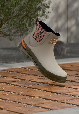 Bottine en caoutchouc beige avec un panneau d'accent texturé à imprimé léopard coloré et des détails orange, dotée d'un bout rond et de semelles plates.