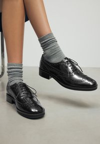 Scarpe brogue nere in pelle lucida verniciata, design con lacci, tomaia testurizzata e tacco basso a blocco. Abbinati a calzini grigi a coste.