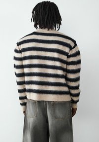 Sweter w paski z szerokimi czarnymi i beżowymi pasami, o miękkiej teksturze i skróconym kroju. Połączony z luźnymi, wyblakłymi szarymi dżinsami.